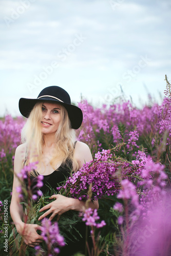 beautiful girl in black dress and hat standing in a field of lupine flowers