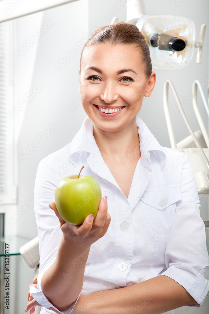 Portrait of beautiful female doctor in white uniform smiling and holding green fresh ripe apple. Face expressions, emotion, health care, medicine, occupation Portrait of beautiful female doctor in white uniform smiling and holding green fresh ripe apple. Face expressions, emotion, health care, medicine, occupation