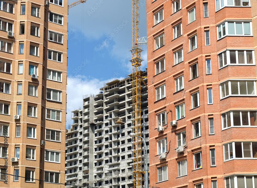 Urban scene. Construction of city district. Constructed brick houses in the foreground and construction of concrete building on the far. Photo in sunny day