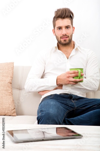 A young adult man sitting on couch with coffee..