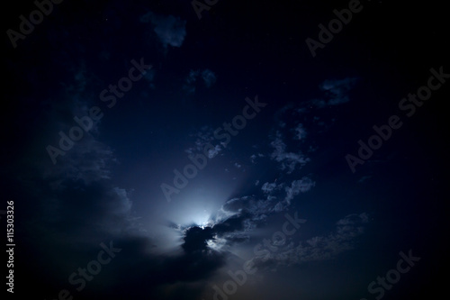 The moon behind the clouds in the night sky.