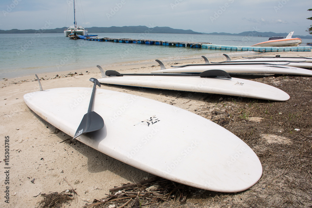 Soft focused of white Surf board on the beach and black surf board paddle on top with Andaman ocean background at Koh Naka Yai,Phuket ,Thailand Soft focused of white Surf board on the beach and black surf board paddle on top with Andaman ocean background at Koh Naka Yai,Phuket ,Thailand