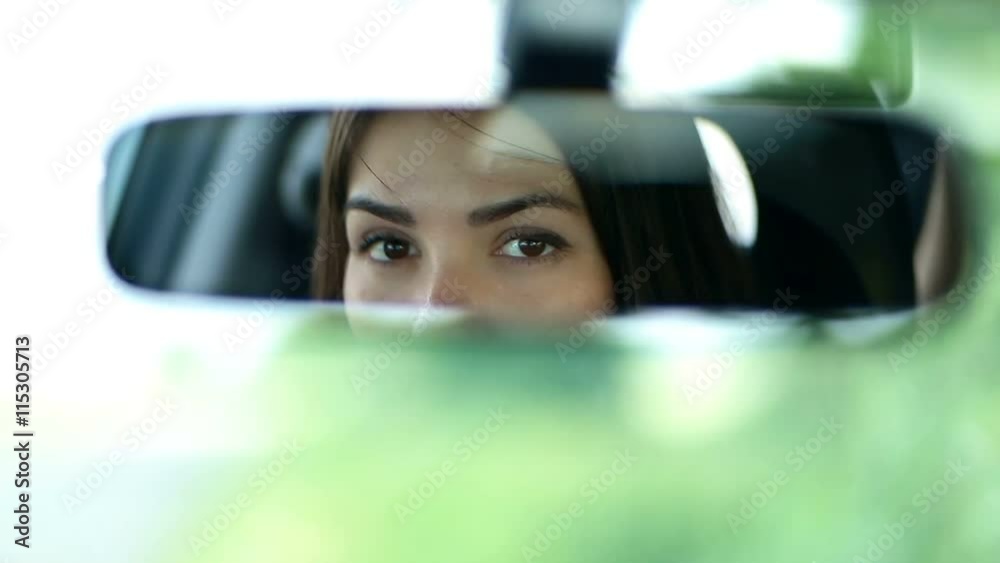Young beautiful woman looking in rearview mirror