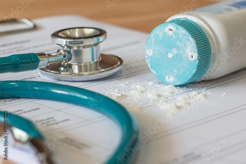 Baby powder product with talc mineral spilling over diagnosis record paper on doctor's pad with stethoscope photo