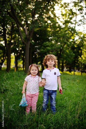 little boy and girl holding hands on the green background. brother and sister holding hands with toys