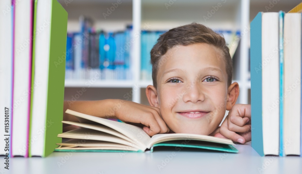 Schoolboy sitting on table and reading book in library Schoolboy sitting on table and reading book in library