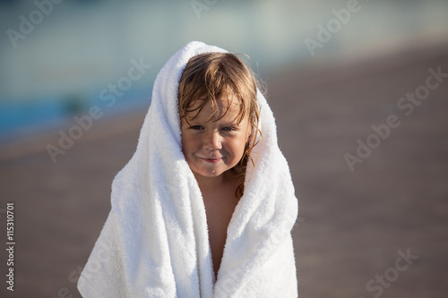 Cute child with white towel after swimming in pool

