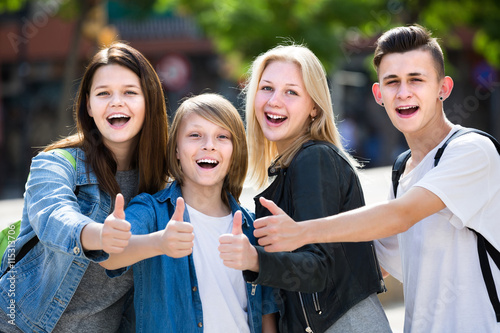 Portrait of four teenagers standing and holding thumbs up togeth