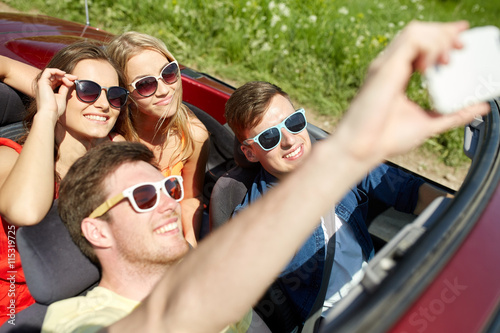 friends driving in cabriolet car and taking selfie