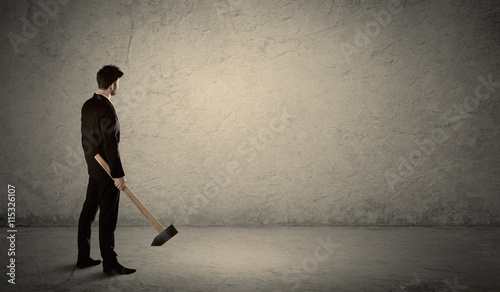 Business man standing in front of a grungy wall with a hammer