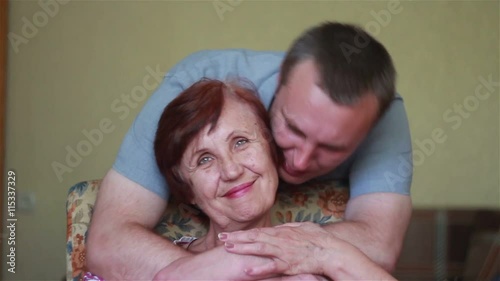 son approaches and gently hugging elderly mother