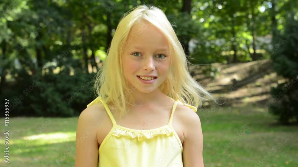 little happy cute girl stands in the evegreen park and smiles to the camery - eye contact - close up