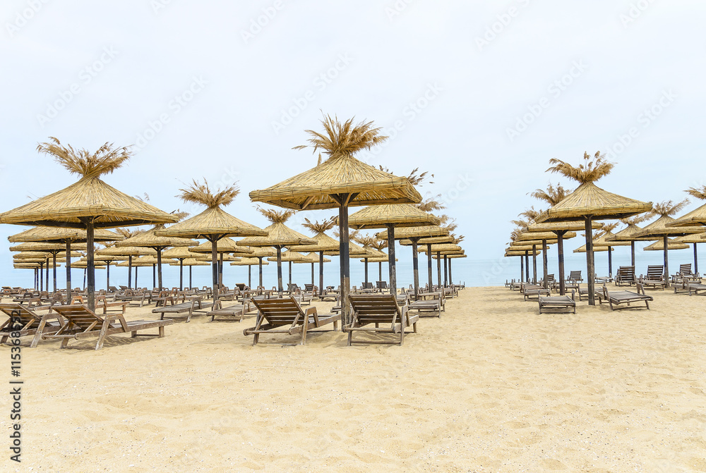Thatched umbrellas and wooden lounge chairs on the beach.