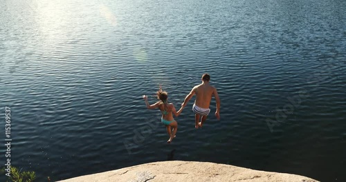 Happy Young Adult Couple Holding Hands Jumping Into Lake 