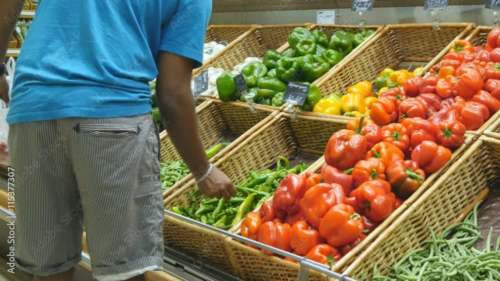 Indian man is choosing peppers in a grocery supermarket. Guy  selecting fresh ripe green peppers in grocery store produce department. Rear view