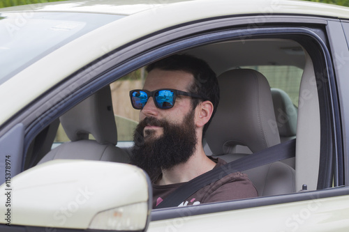 Young man with a beard and sunglasses driving his car.