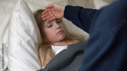 Young caucasian female sick in bed with mother checking for a fever. 