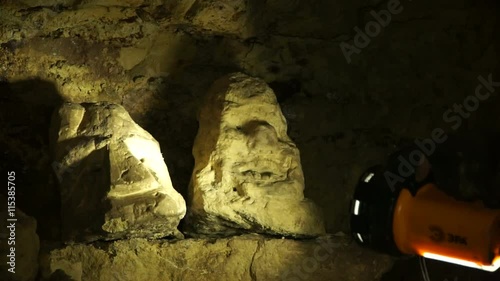 Underground researchers climb in an underground tunnel. Passing by the stone heads.