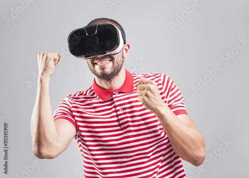 Excited young guy using a VR headset on gray background