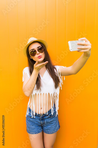 Fashion happy woman makes self portrait on smartphone  over city color wall background