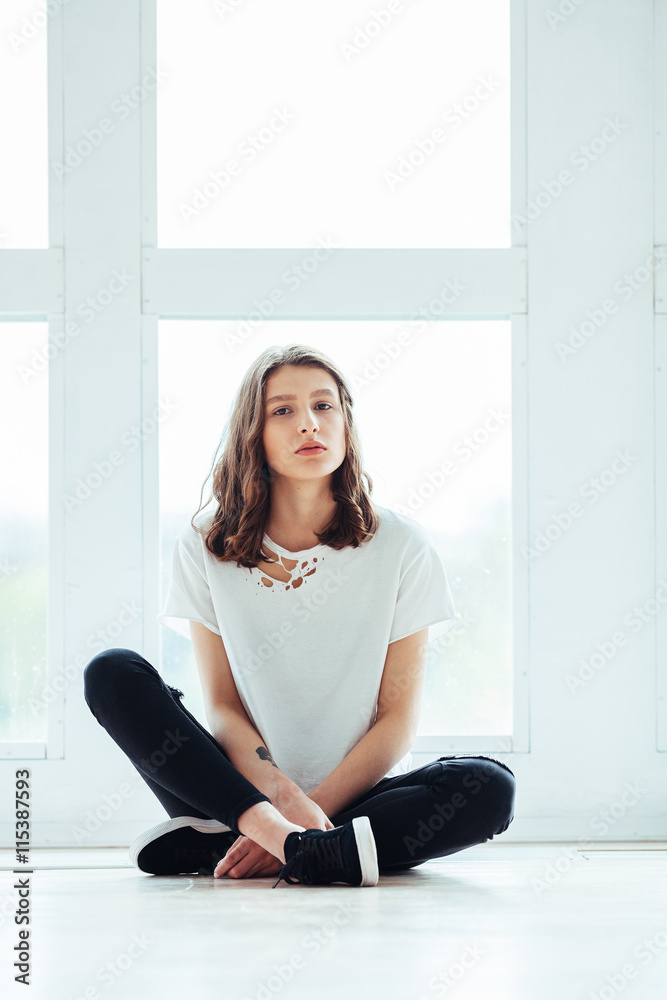 Lost in thoughts. Young beautiful brunette hipster woman sitting on floor near huge window and looking away