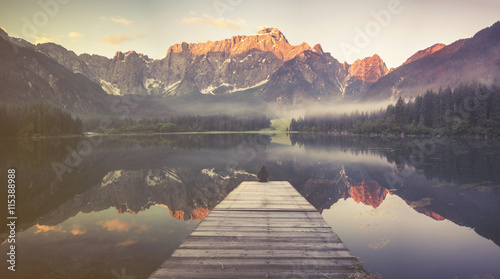 Sylwetka mężczyzny siedząca na drewnianym pomoście w sceneri pięknego,górskiego jeziora