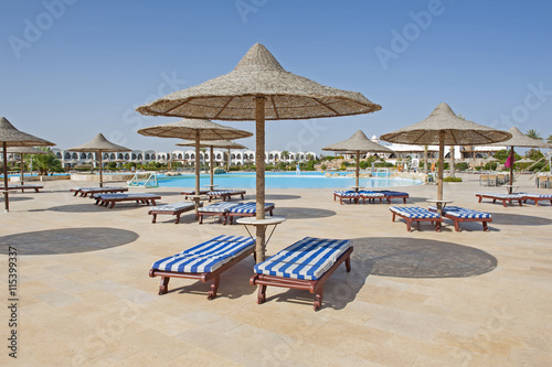 Sunbeds and parasols by a tropical hotel resort swimming pool