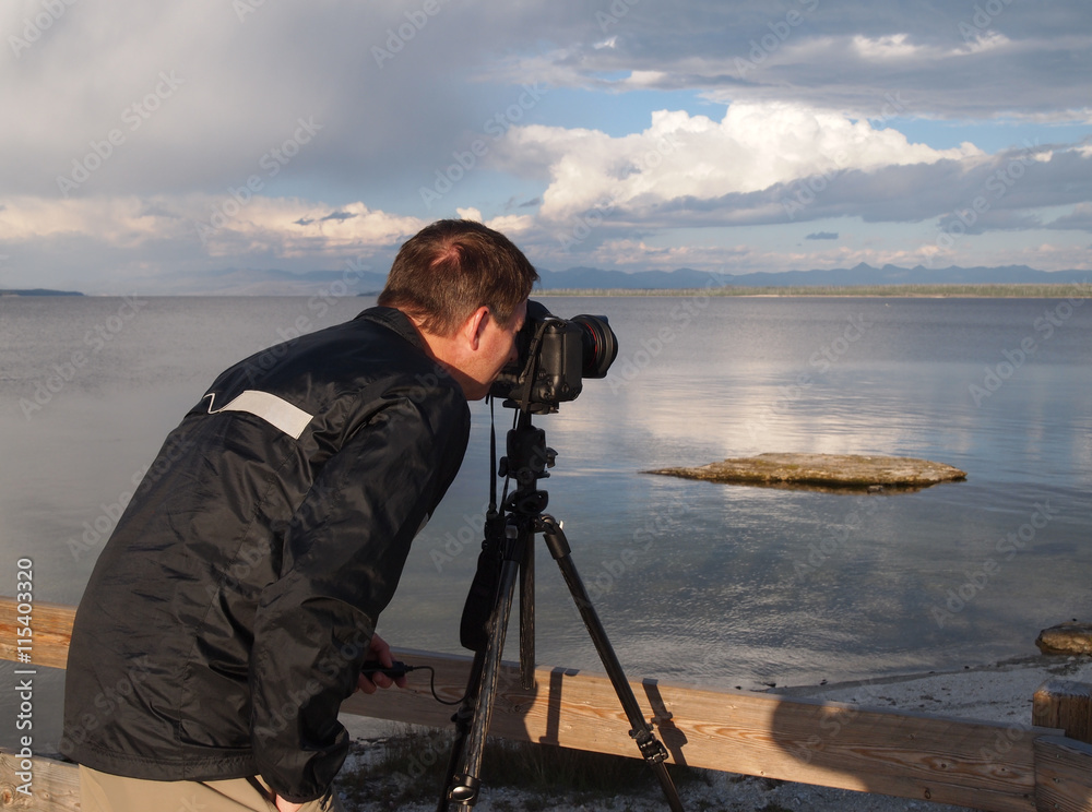 Man taking photo of lake with camera mounted on tripod