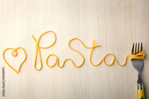 Word PASTA made of cooked spaghetti with fork on wooden background