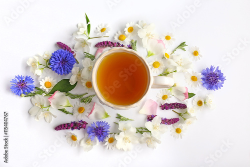Cup of tea with fresh flowers lying around on white background