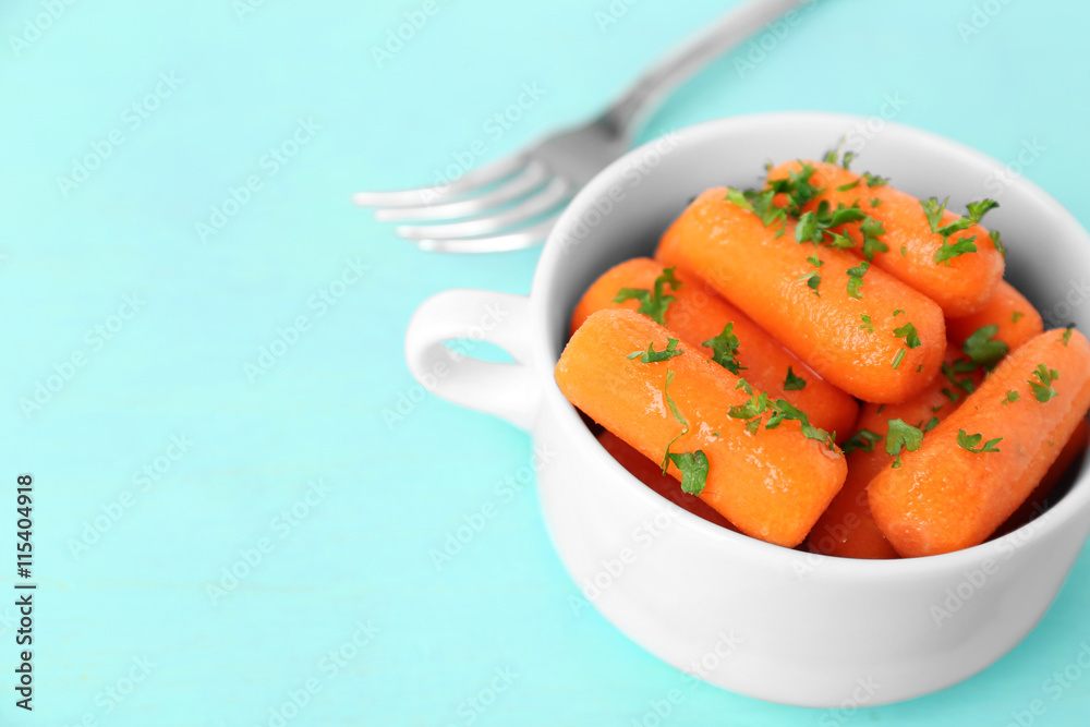 Small baby carrots in soup plate on light blue background Small baby carrots in soup plate on light blue background