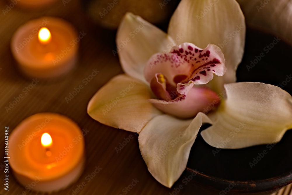 Beautiful orchid flower in wooden bowl and candles on wicker mat