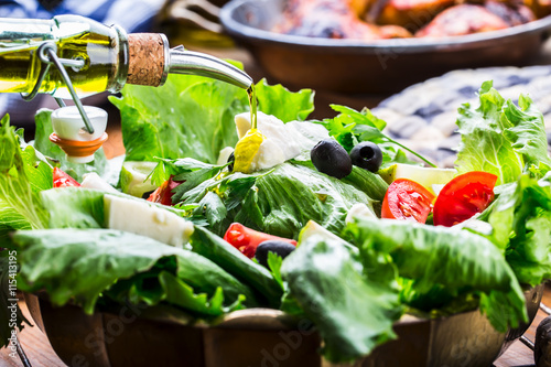 Vegetable lettuce salad. Olive oil pouring into bowl of salad. Italian Mediterranean or Greek cuisine. Vegetarian vegan food.