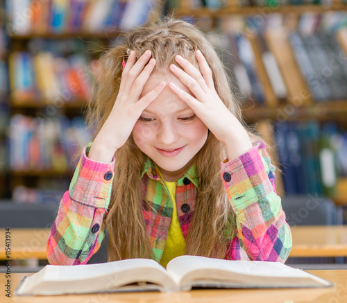 Tableau sur toile Happy girl reading a book in the library