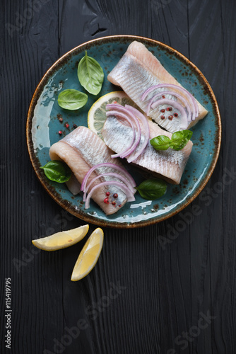 Glass plate with herring fillet on a black wooden background