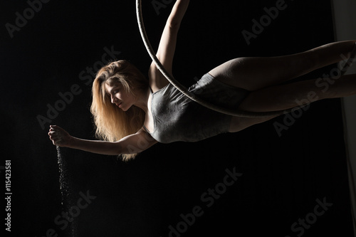 Acrobatic woman hunging on aerial hoop and pouring flour photo