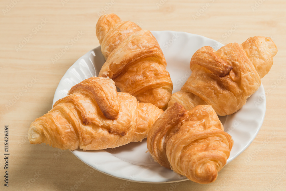four gold croissant in white plate on wood table four gold croissant in white plate on wood table