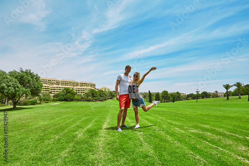 Young couple standing on a green field. Happy couple man and woman on the golf course. Blue sky and houses in the background.