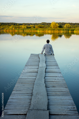 Alone man sitting on the edge of a pier on the lake