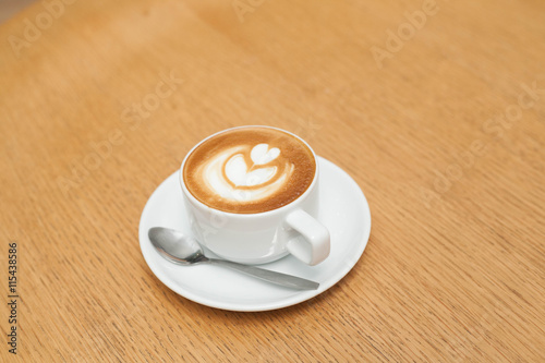 A cup of coffee with heart pattern in a white cup on wooden background  