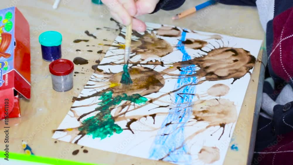 Child at School Sitting at the Desk Draws With a Brush Green and Brown Colors, Closeup Child at School Sitting at the Desk Draws With a Brush Green and Brown Colors, Closeup