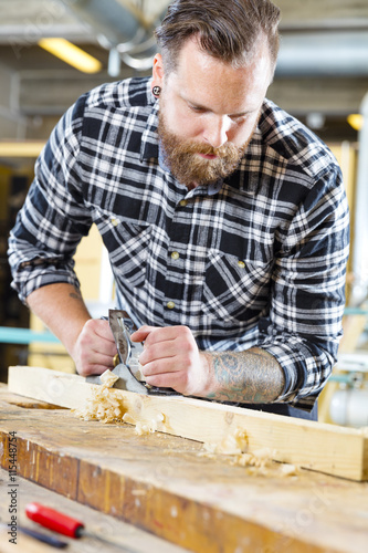Carpenter work with planer on wood plank in workshop