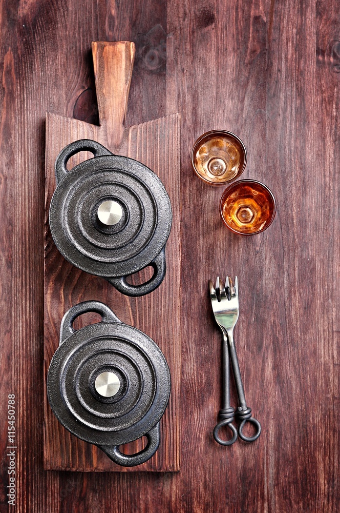 Fototapeta premium The small cast iron pan with forks and glasses on a cutting board