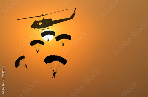Silhouette of parachute and helicopter on sunset background
