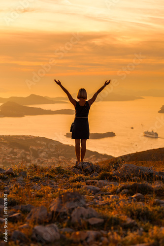 Female tourist standing on the background of Bay at sunset. Misty layers of islands. Sunset in Adriatic sea with layers mountains on the horizon. Hills, growing out of the water. Dubrovnik. Croatia.