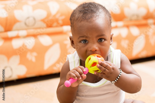portrait d'un bébé assis portant à la bouche son jouet photo