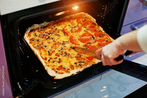 Woman cut with a knife homemade pizza in electric oven in the kitchen
