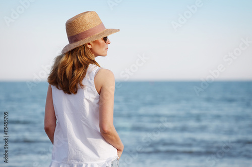 Peaceful and relaxing summer day at seaside. Mature woman standing on beach.