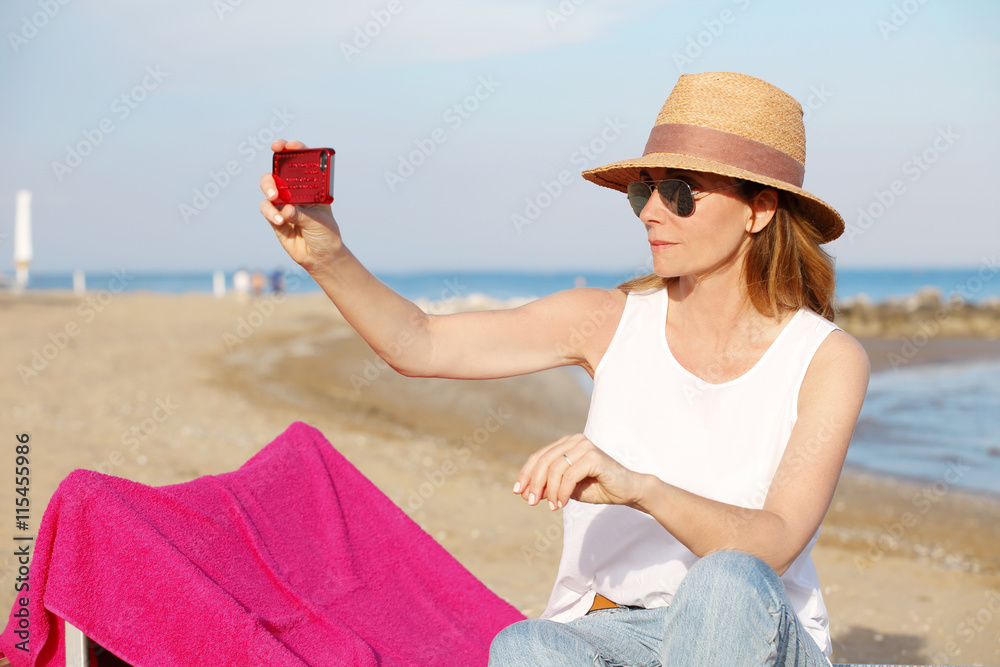 Relaxing on the beach. Middle age woman taking a selfie with mobile phone at seaside.