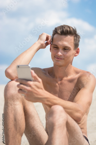 Young athletic man with cellphone on the beach